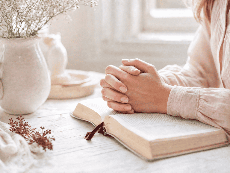 Woman praying peacefully with hands folded over an open Bible for her son's faith using 29 bible verses for son praying scripture over your teen