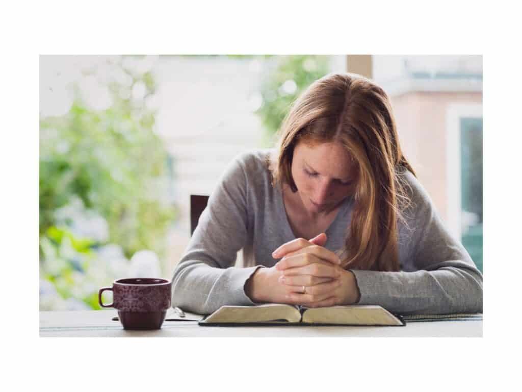 Woman sitting at table praying over her Bible featured image for 45 Powerful Bible Verses and Songs for Encouragement during Hard Times