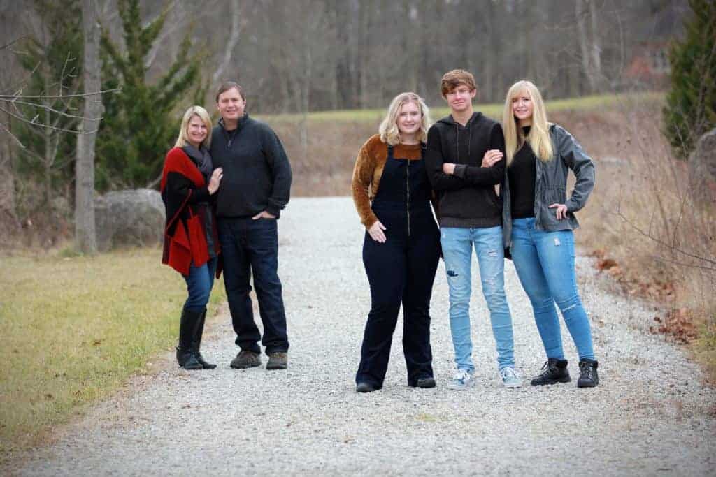 couple standing behind their older teenage children on a gravel driveway